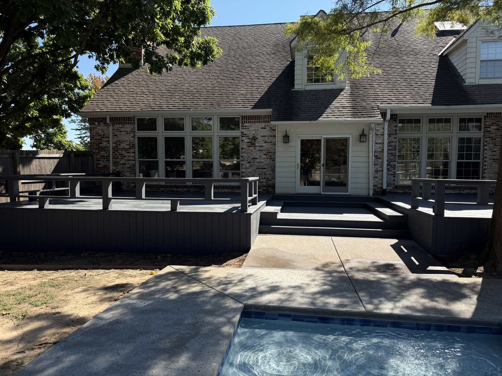 Dark composite deck with pool and multi-level seating built by Deck Hoss