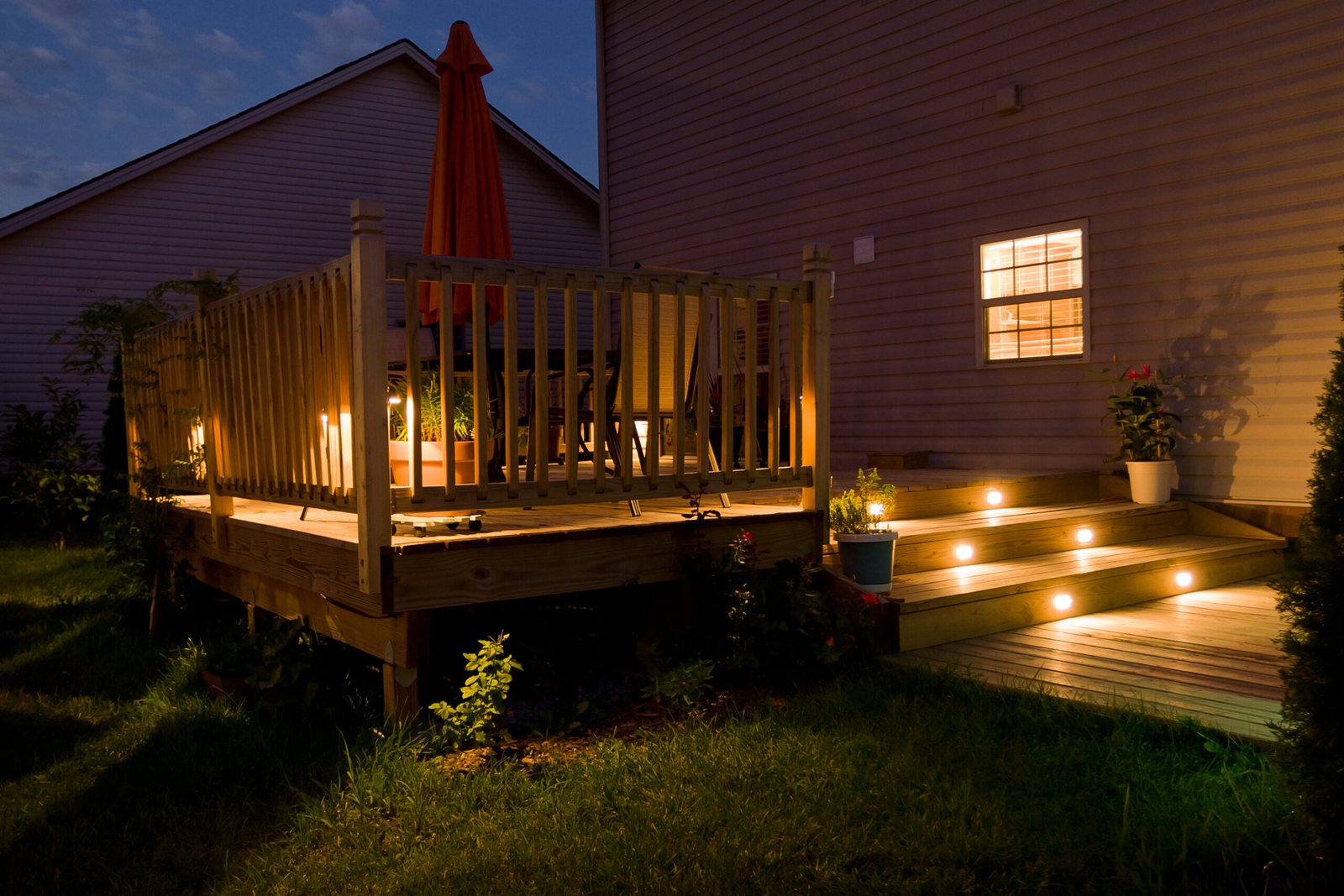 Wood deck with railing and built-in lighting at dusk behind a two-story home