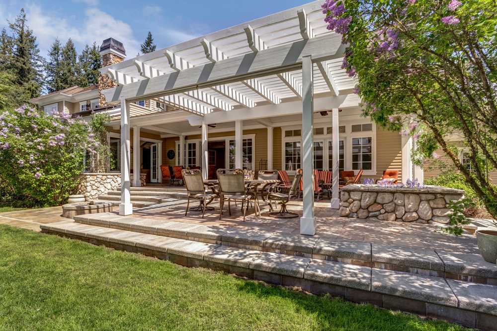 Attached covered structure with white columns over a patio seating area behind a two-story home
